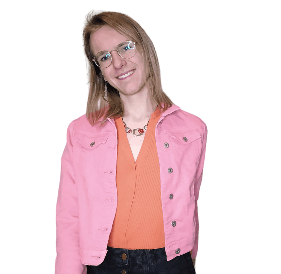 A photo of Jenny. She's in frame from head to hips. She has blonde straight shoulder-length hair and wears round glasses and long earrings. She wears an orange blouse with a pink denim jacket and a red-metal coloured necklace. She's posing as if she's walking, looking into the camera with her head tilted a little and smiling.
