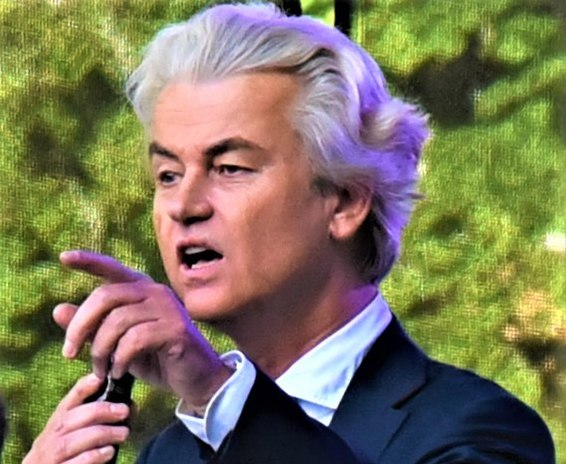 Geert Wilders pointing and speaking into a microphone with an angry look