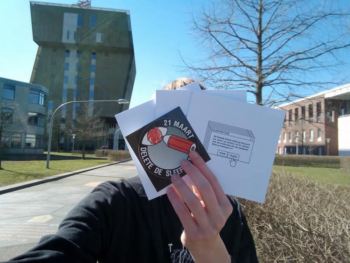 Tyler at the Zernike Campus in Groningen, holding flyers and stickers in front of their face.