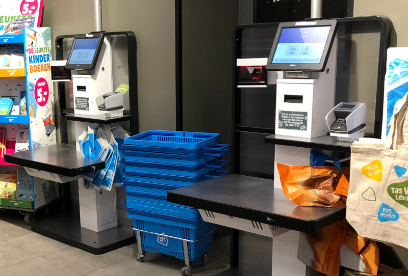 A photo of two self-service checkout registers from Albert Heijn, with a stack of baskets standing inbetween them.