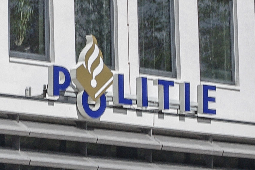 Een foto van een bord van het logo van de politie, op de gevel van een gebouw.